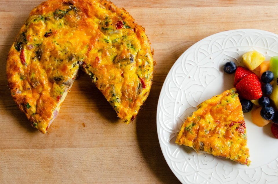 A frittata on a board with a wedge cut out on a white plate.