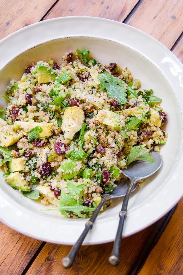 Quinoa salad with artichokes and dried cherries in a white bowl on a wooden table.