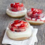 Mini Sous Vide Strawberry Cheesecakes in jars on a wooden table with a white napkin.