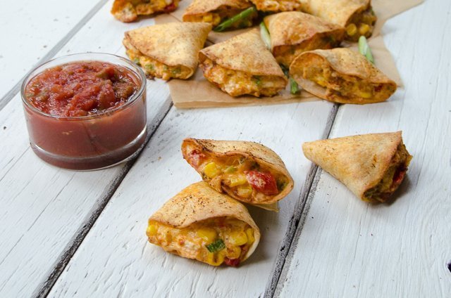 Air-fried chicken stuffed tortillas on a white wooden table with a little jar of salsa.