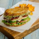 California Turkey Club Sandwich on a wooden board with sweet potato chips on the side.