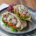 Turkey Waldorf Salad Pita on a stone plate with a striped placemat and grapes on the side.