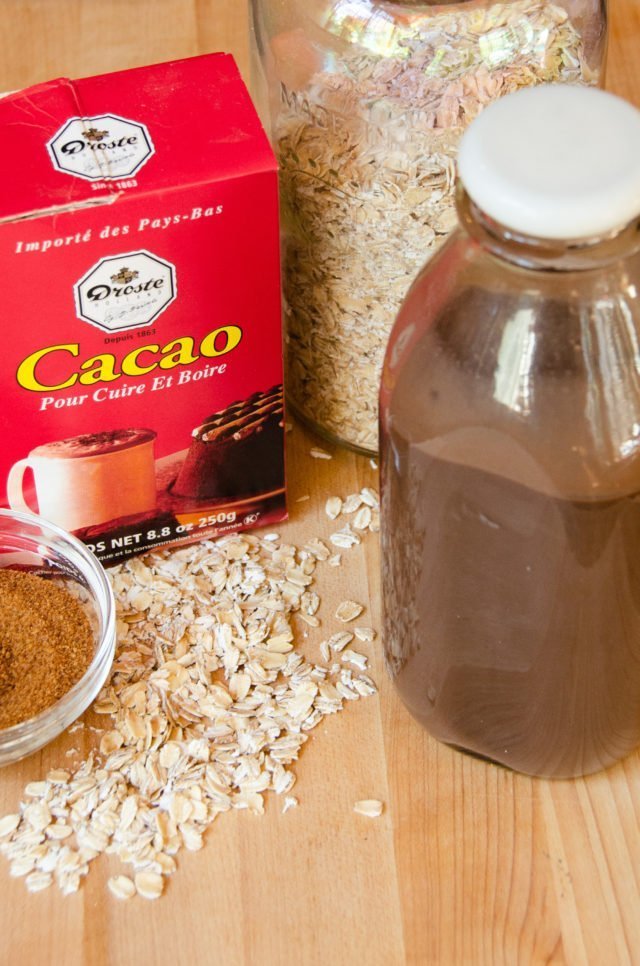 A bottle of homemade chocolate oat milk with cocoa powder and rolled oats in the background.
