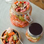 Giardiniera in jars on a table with a little wooden bowl and spoon.