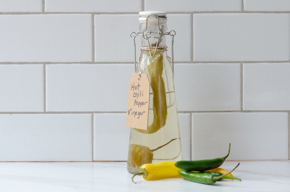 Homemade flavored vinegar - Hot Chili pepper vinegar on a counter with some hot peppers.