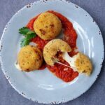 Arancini in a pool of tomato sauce on a blue plate.