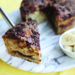 Banana cake with chocolate chunks on a marble cake plate with a yellow background.