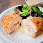 Chicken Cordon Bleu on a plate with brandy cream sauce poured on top and a side salad.