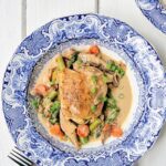 Chicken fricassee in a blue and white bowl on a white wooden table.