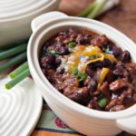 Chili con carne in a white oval dish with scallions on the side.