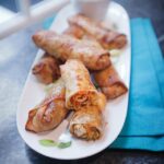 Shrimp Egg Rolls on a plate with a turquoise napkin next to a window.