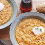 Two bowls of yellow split pea soup with a cruet of maple syrup.