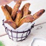 Dill fried pickles in a parchment lined wire basket with dipping sauce on the side.