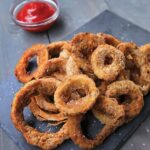 Beer Battered onion rings on slate on a wooden table with ketchup.