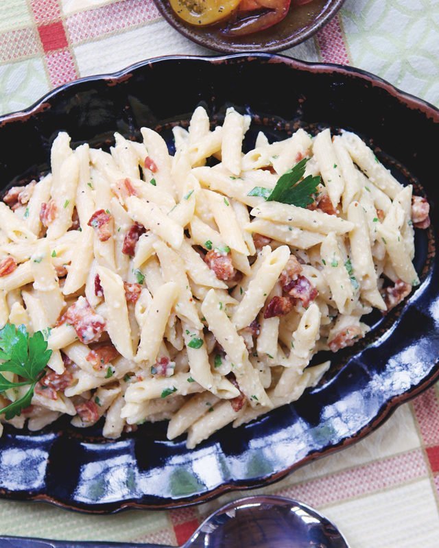 Penne Carbonara pressure cooker on black tray with tomatoes on one side.