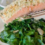 A piece of baked salmon with horseradish crust being placed on a bed of wilted spinach.