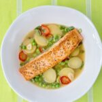 Salmon with potatoes and peas in a white bowl on a lime green tablecloth.