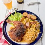 Summer Ale Chicken on a blue rimmed plate with corn and potatoes, a glass of beer and a bottle opener.