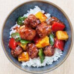 Sweet and sour pork in a blue bowl on a peach placement.