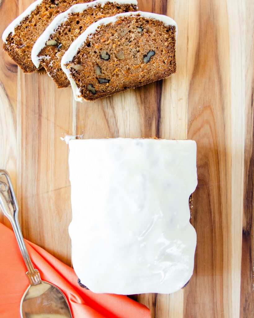Carrot Cake Loaf with Cream Cheese Icing on a cutting board with three slices cut.