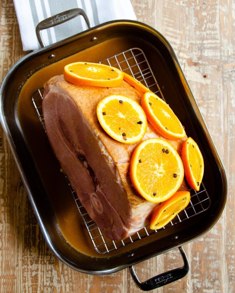 Ham studded with oranges and cloves in a roasting pan.