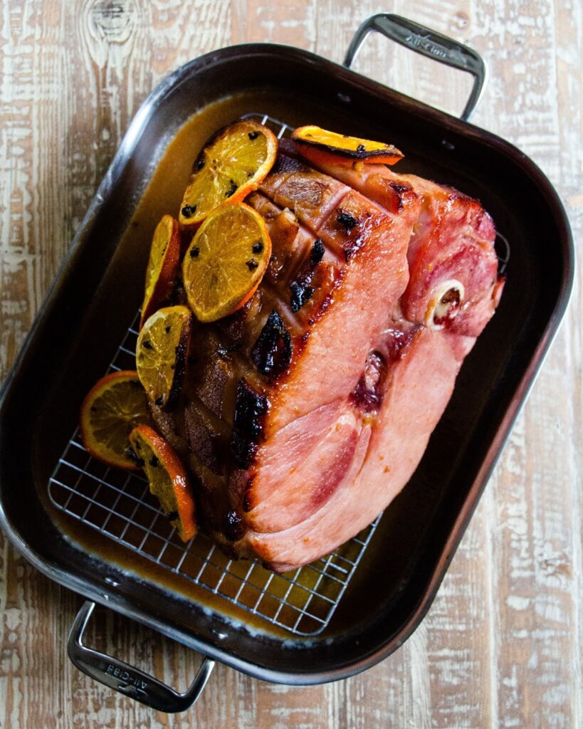 Baked ham studded with oranges and cloves in a roasting pan.