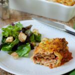 Lasagna Roll Ups on a plate with salad with the full casserole behind.
