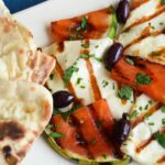 Grilled cheese and watermelon with olives, mint and grilled bread on a white platter.