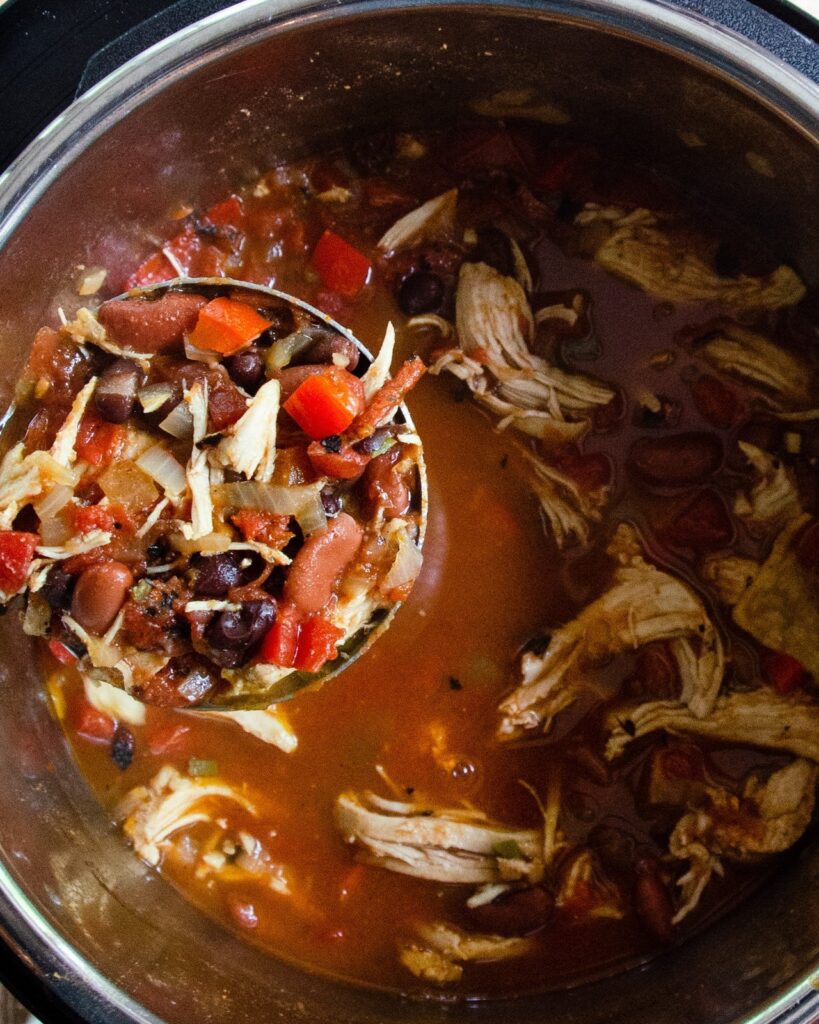Chicken tortilla soup in a pressure cooker with a ladle spooning some out.
