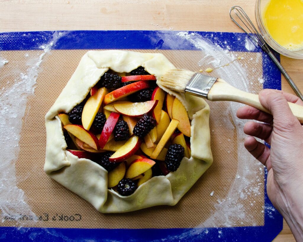 Easy Fruit Tart on a baking mat, uncooked with egg wash being brushed on.