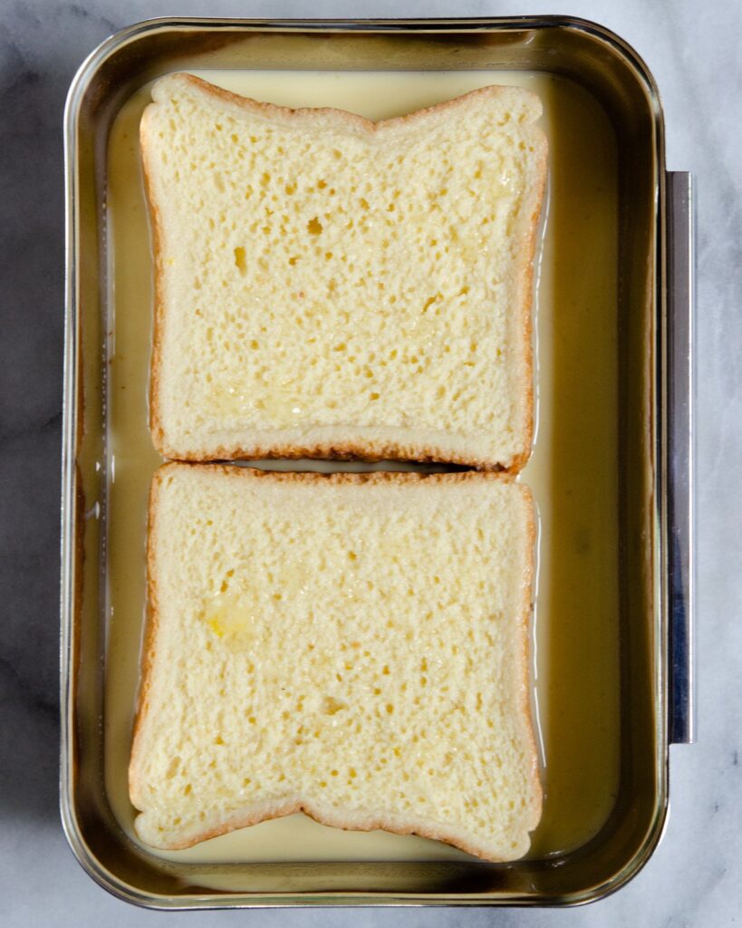 Square pieces of bread soaking in egg custard.