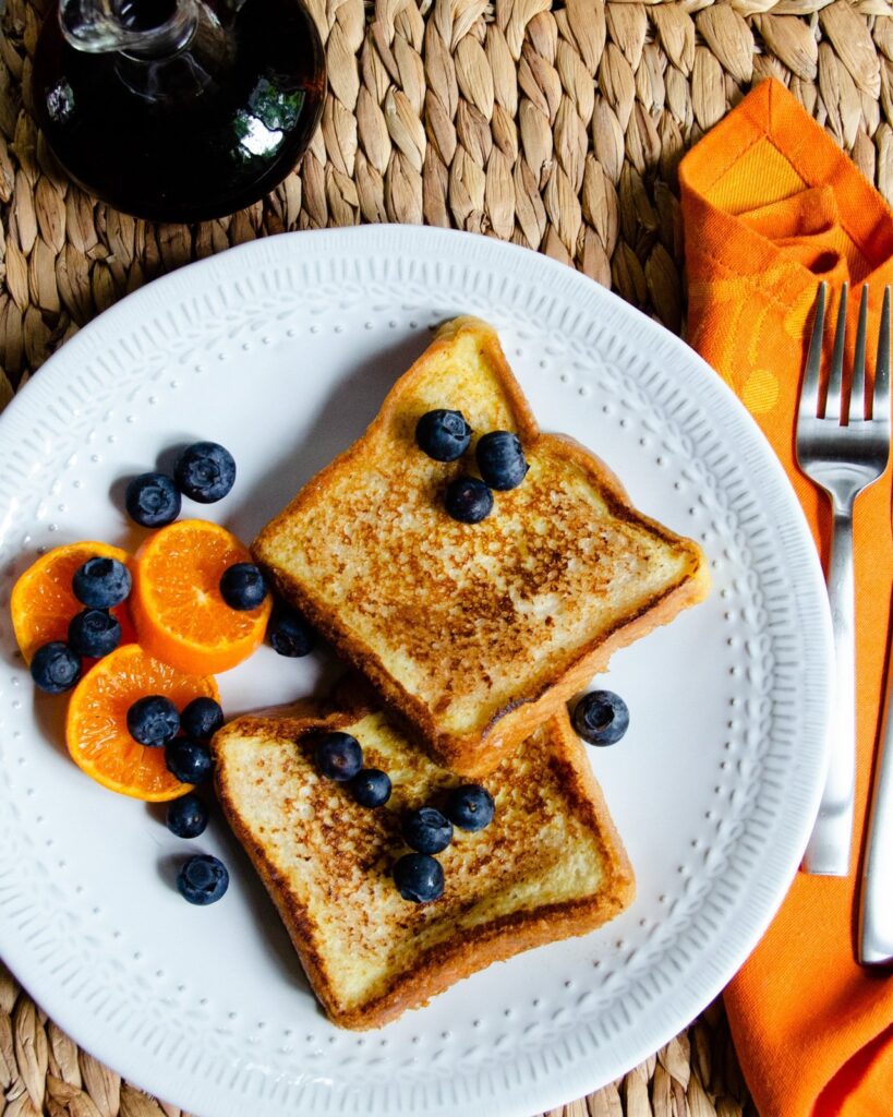 French toast with blueberries and mandarins on a white plate with orange napkin.