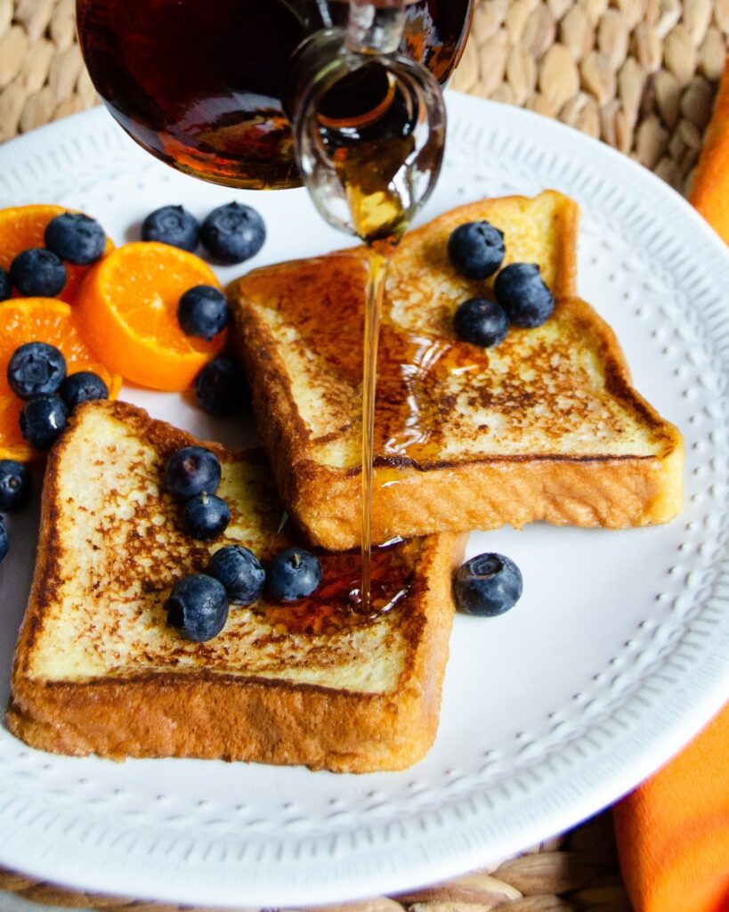 French toast with blueberries and mandarins and maple syrup being poured on top.