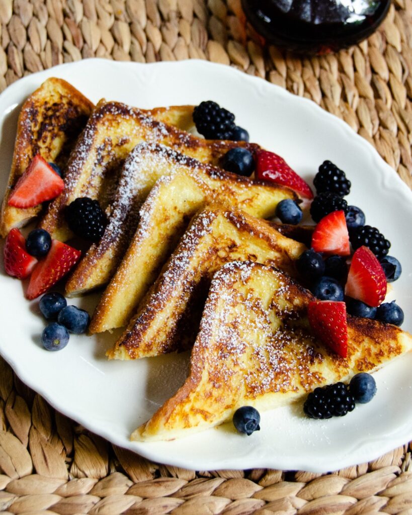 French toast cut into triangles on a white plate with raspberries and blueberries.