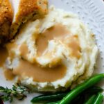 Gravy poured over mashed potatoes with green beans and chicken.