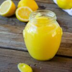 Lemon Curd in a jar with a spoon and some lemons around.