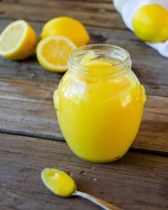 Lemon Curd in a jar with a spoon and some lemons around.