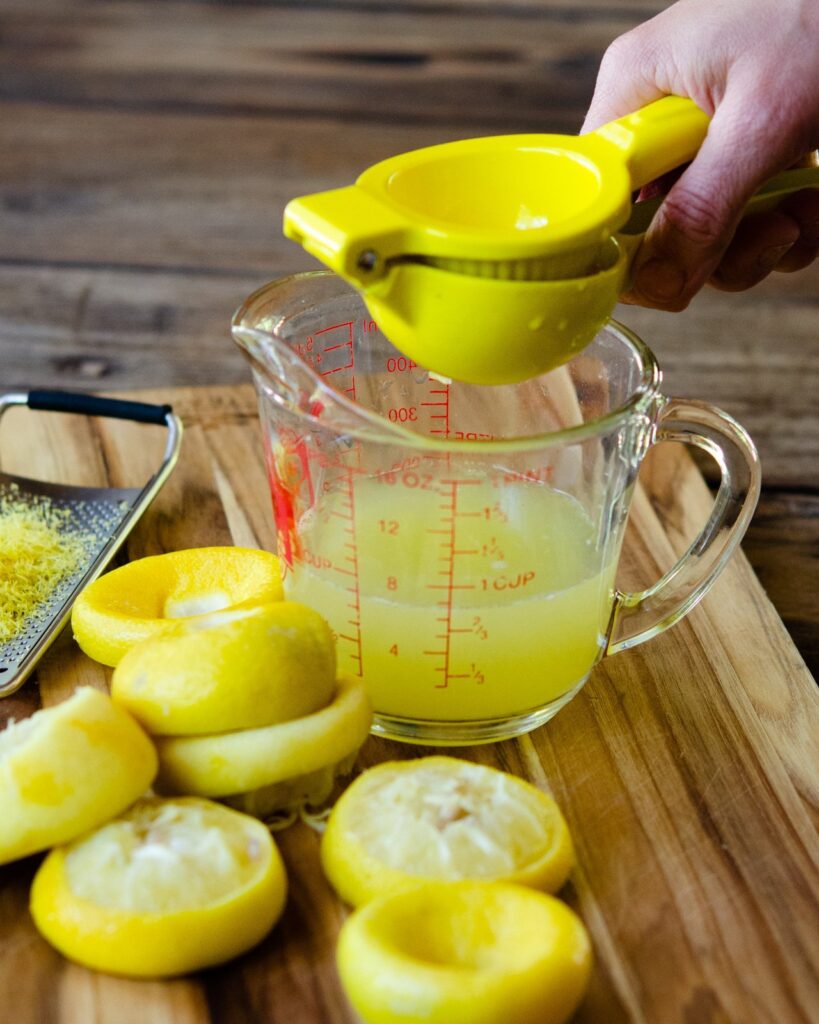 A hand juicing lemons into a measuring glass.