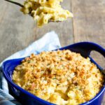 A spoon lifting baked mac and cheese out of a blue casserole.