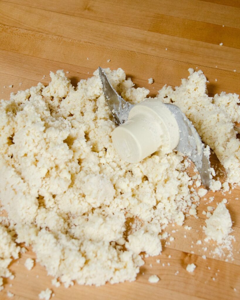 Pastry in crumbs with a food processor blade on a wooden work surface.