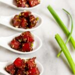 Four spoons of tuna poke on white marble with scallions along side.