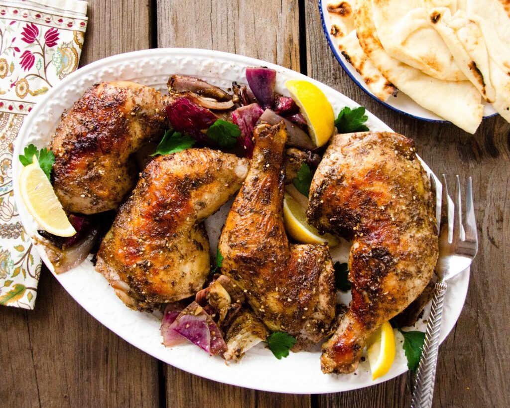 Za'atar chicken legs on a white platter with bread.