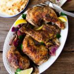 Za'atar chicken legs on a white platter with serving fork and bread on a wooden table.