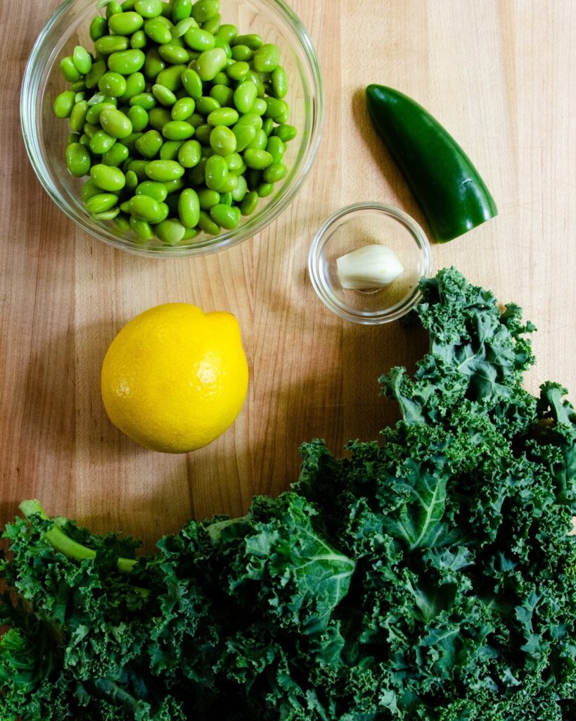 Ingredients for edamame-kale dip on a wooden cutting board - edamame, kale, lemon, garlic and jalapeño pepper.
