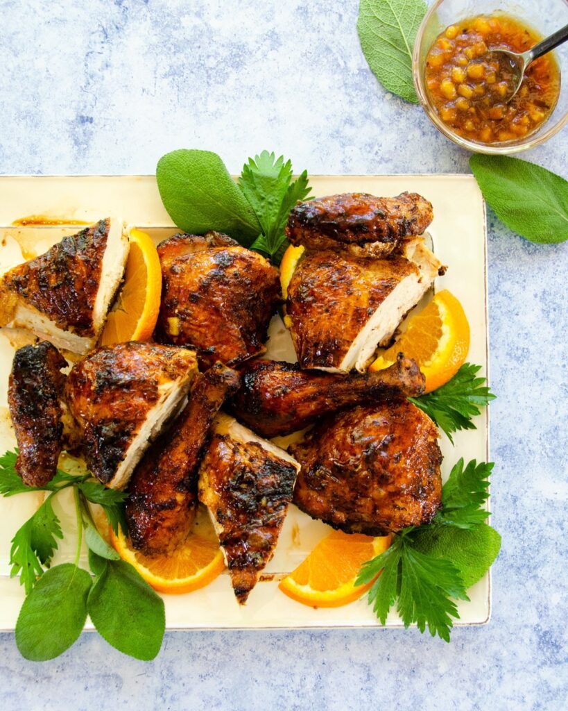 Grilled Spatchcocked chicken on a platter with herbs and orange.