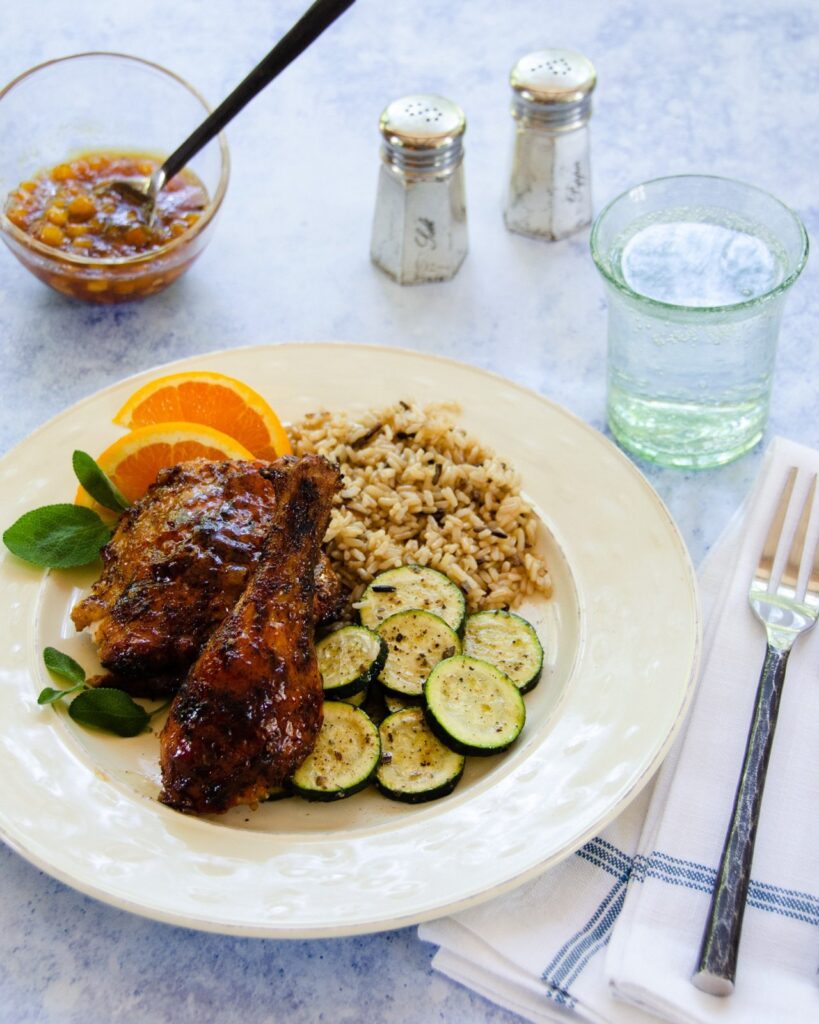 A dinner plate with chicken, zucchini and wild rice on a table with place setting.