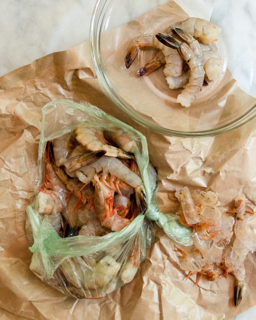 shrimp in various stages of being peeled and deveined on brown paper.