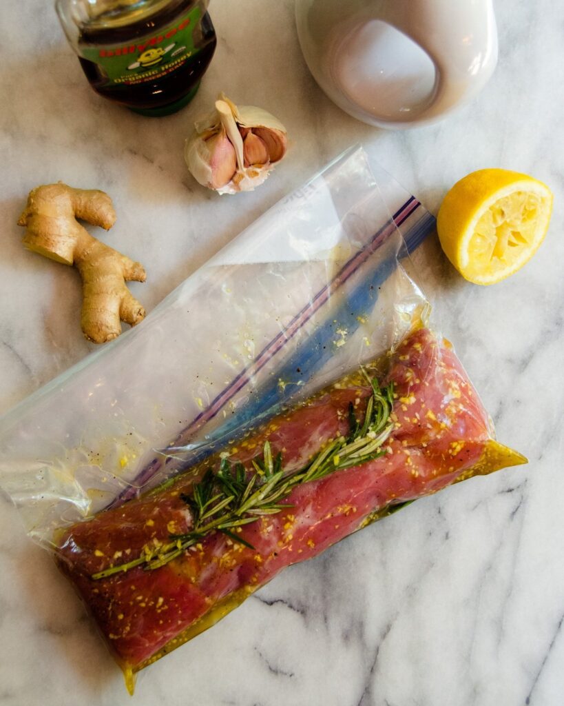 Pork tenderloin in a bag with rosemary, ginger, garlic, honey and lemon on a marble countertop.