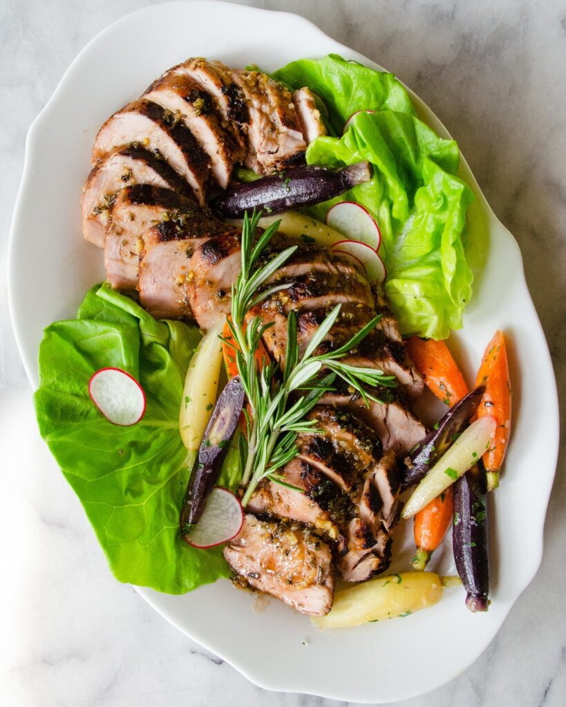 Sous vide pork tenderloin sliced on a white platter with carrots.