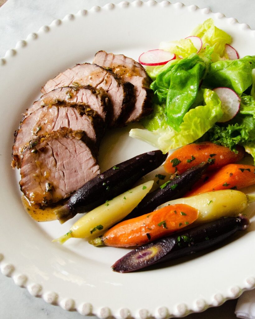 Sous vide pork tenderloin with carrots and a side salad on a white plate.